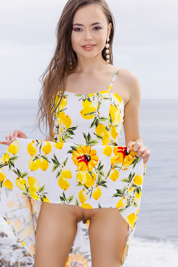 Li Moon in lemon print dress on rocky cliffs, posing solo by the ocean breeze and sun