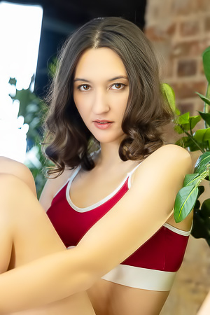 Colette Kai kneels and poses topless in red lingerie before a mirror, her gaze holding you captive in slow, silent desire