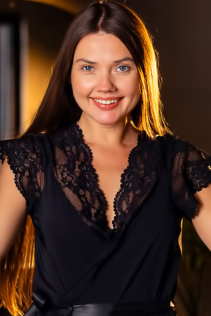 Georgia poses nude and in black lace lingerie, smiling softly in a dim bedroom with mirror reflections
